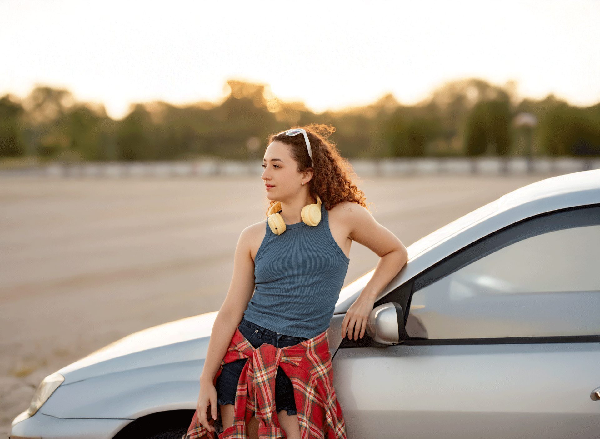 young woman standing by her car at sunset looking into the distance